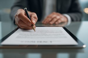 Business professional signing a valid contract displayed on a digital tablet in an office setting.