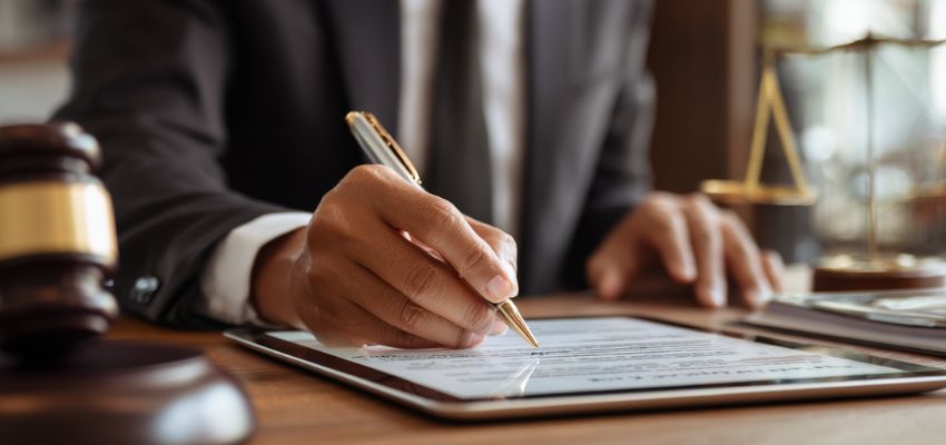 valid-contract3 Lawyer reviewing and signing a valid contract on a tablet with legal scales and gavel nearby.