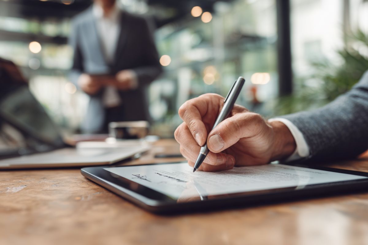 Close-up of a man signing a digital document on a tablet as an authorized signatory.