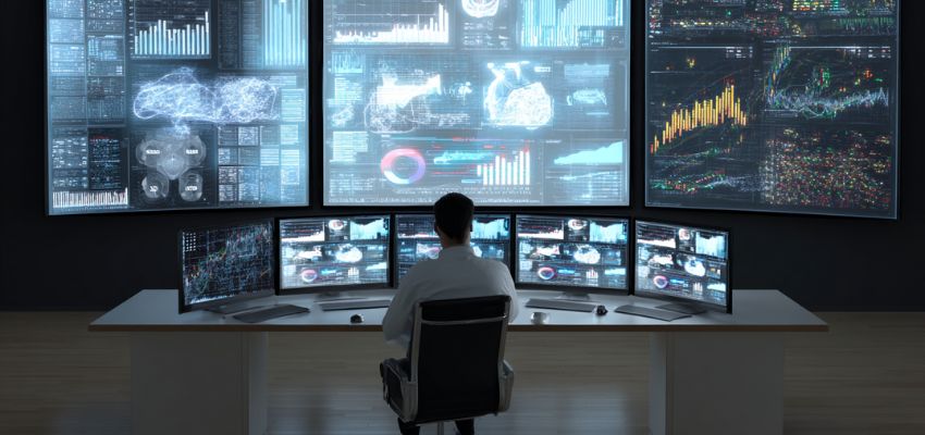 Professional analyst seated at a multi-screen workstation reviewing complex charts, graphs, and data visualizations on large displays during an intensive contract auditing session.