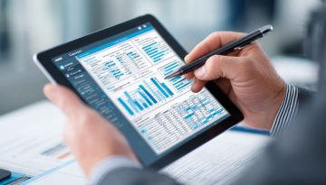 Business professional using a stylus to annotate detailed financial reports and bar charts on a tablet, performing thorough contract auditing for compliance and accuracy.