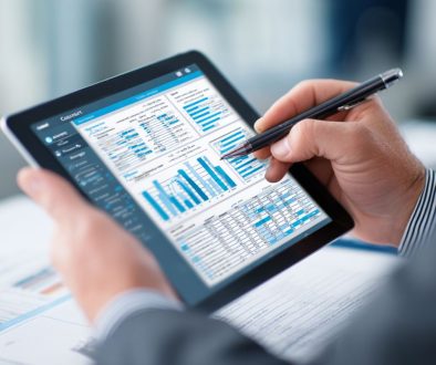 Business professional using a stylus to annotate detailed financial reports and bar charts on a tablet, performing thorough contract auditing for compliance and accuracy.