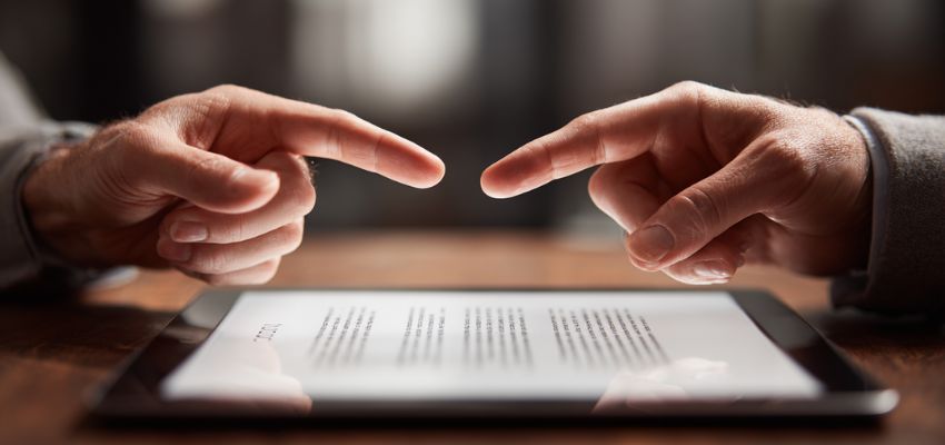 elements-of-contract1 Close-up of two hands pointing at key clauses on a digital contract displayed on a tablet, highlighting the essential elements of contract law.