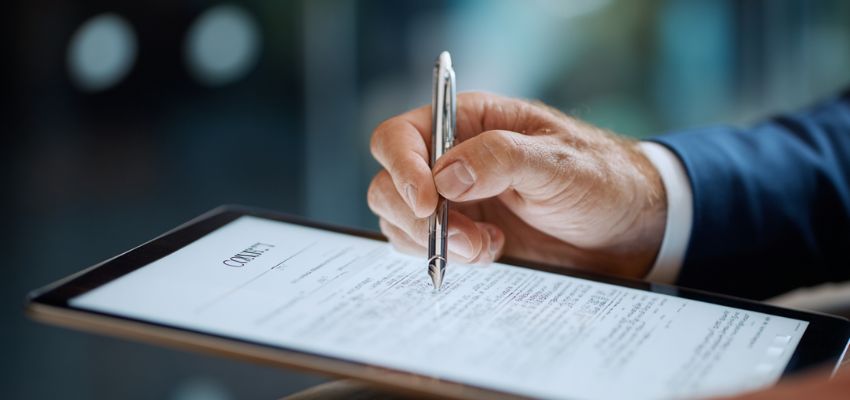 elements-of-contract3 Business professional using a stylus to electronically sign a legal document on a tablet, illustrating the acceptance element of contract formation