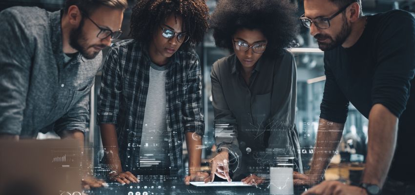 Diverse group of colleagues gathered around a digital touchscreen table analyzing charts and documents together, utilizing contract collaboration software to streamline agreement reviews and approvals.