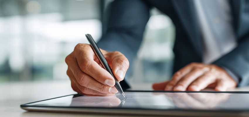 contract-addendum1 A professional in a suit uses a stylus to sign a contract addendum on a digital tablet.
